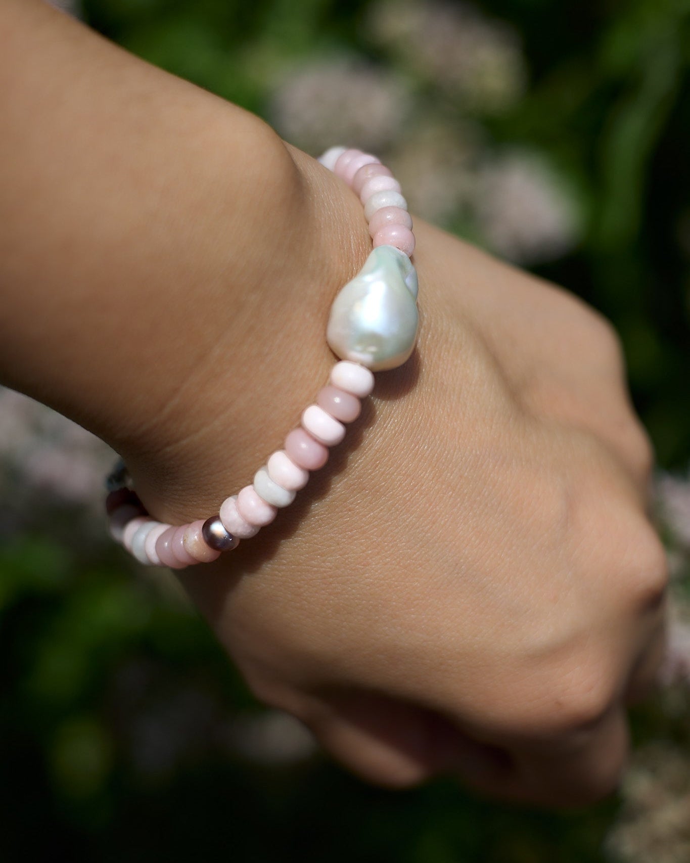Hand wearing a pink and white pearl bracelet with a blurred natural background