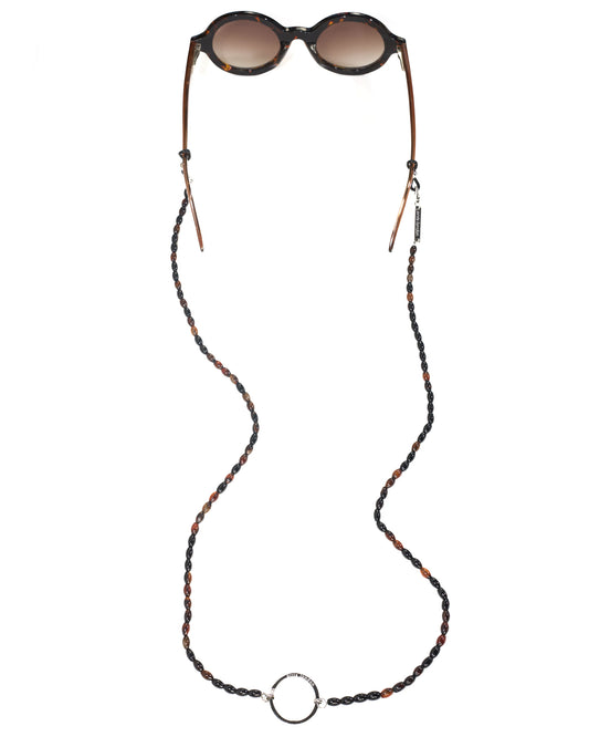 A tortoiseshell-patterned sunglasses chain strap with brown leather tips and a silver-tone ring clasp, shown hanging from round sunglasses on a plain white background.