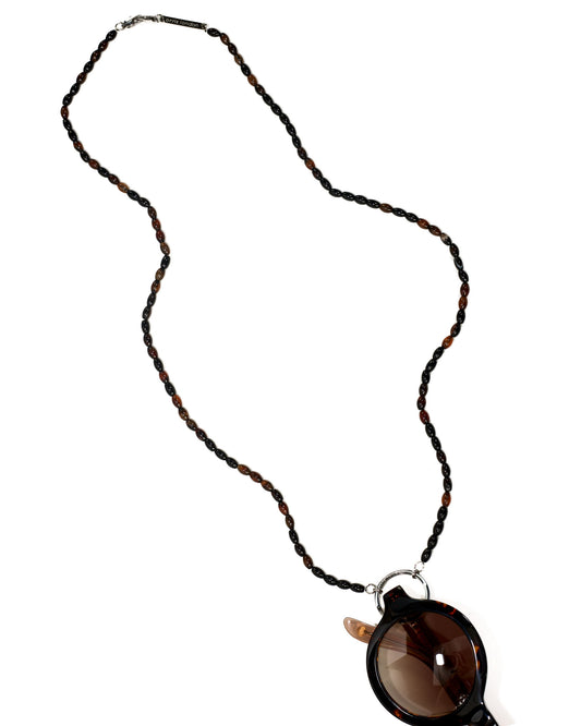A beaded necklace with alternating dark brown and black beads, featuring a large tortoiseshell pendant with brown lenses and silver-tone metal hardware, shown on a plain white background.