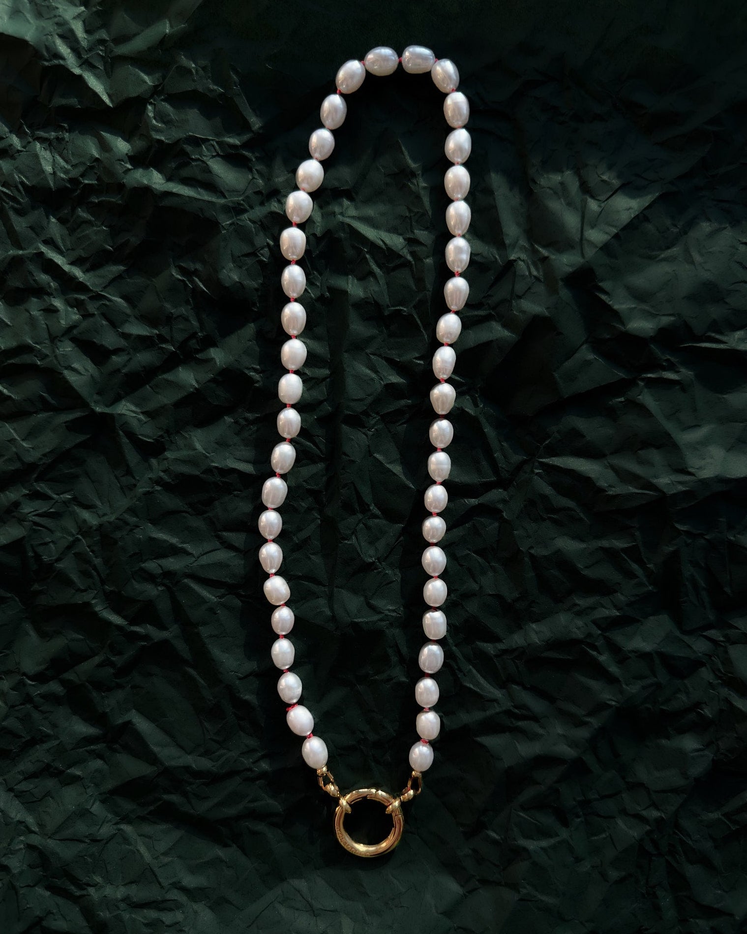 Pearl necklace with a gold clasp on a crumpled green paper background